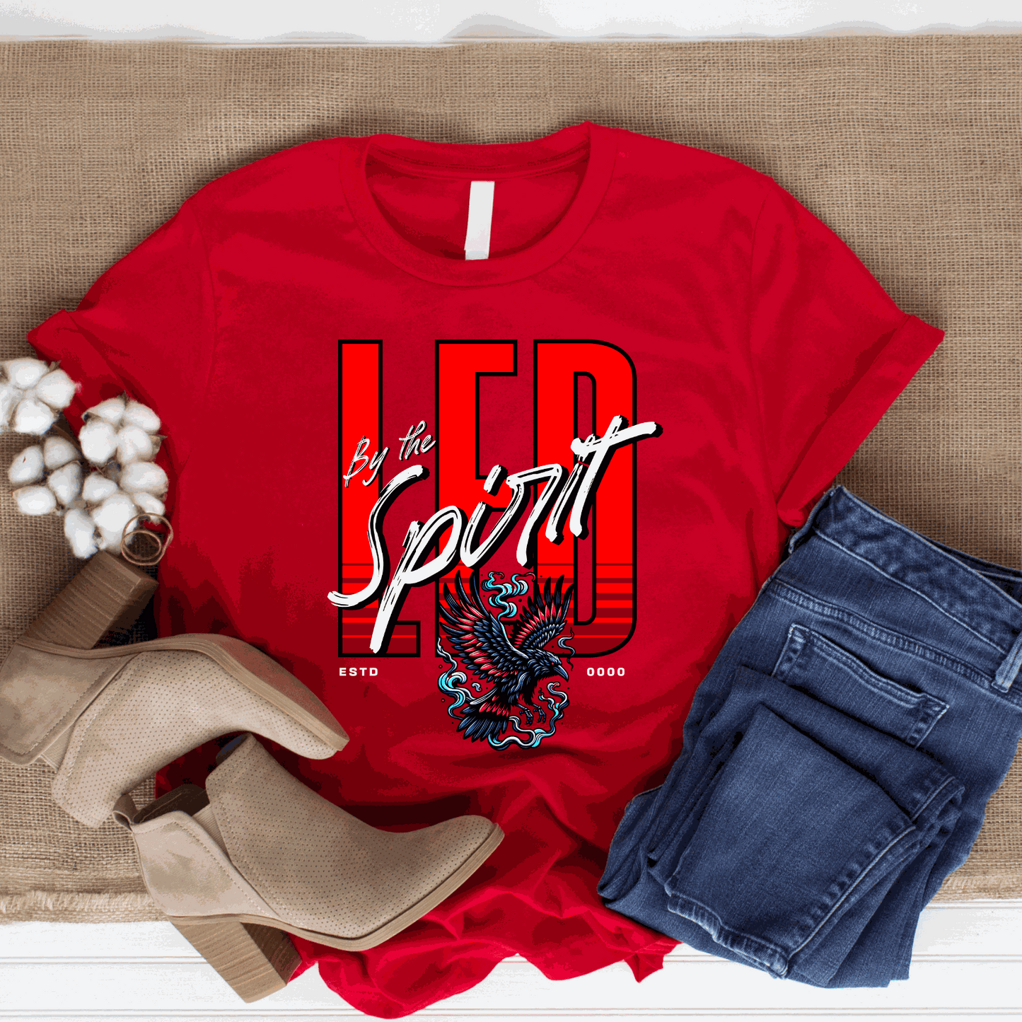 Red Christian LED Unisex T-Shirt with "LED by the Spirit" text and eagle graphic, styled with jeans and beige boots.
