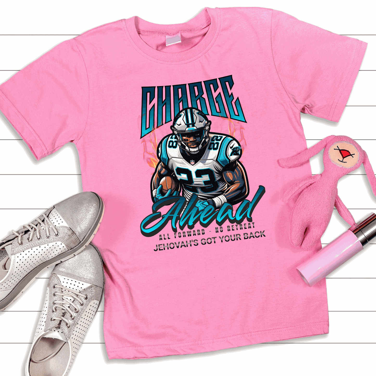 Pink Charge Ahead Unisex T-shirt with football player graphic and motivational text, paired with silver sneaker and pink accessories on white wooden background